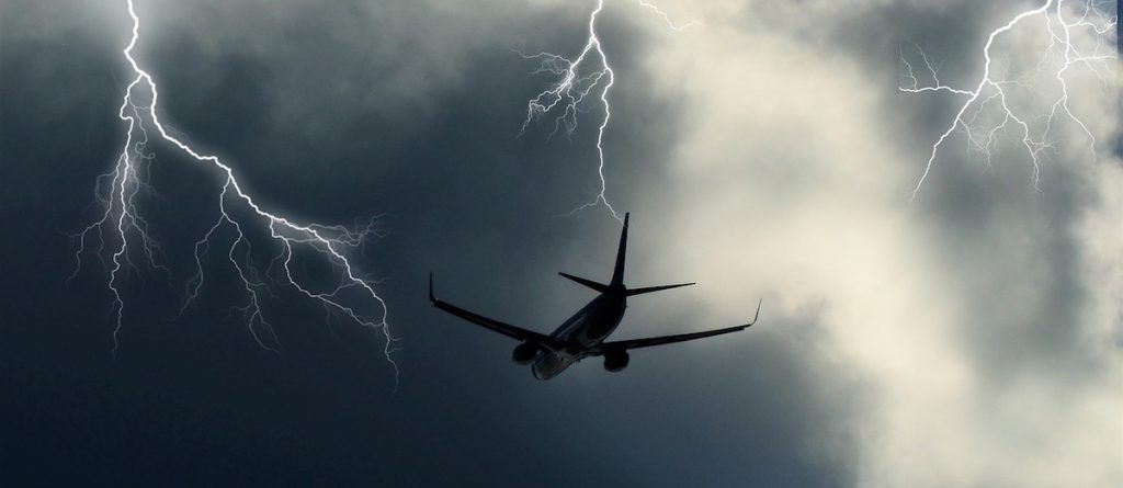 Un avión vuela en un cielo encapotado en el que se distinguen tres rayos.