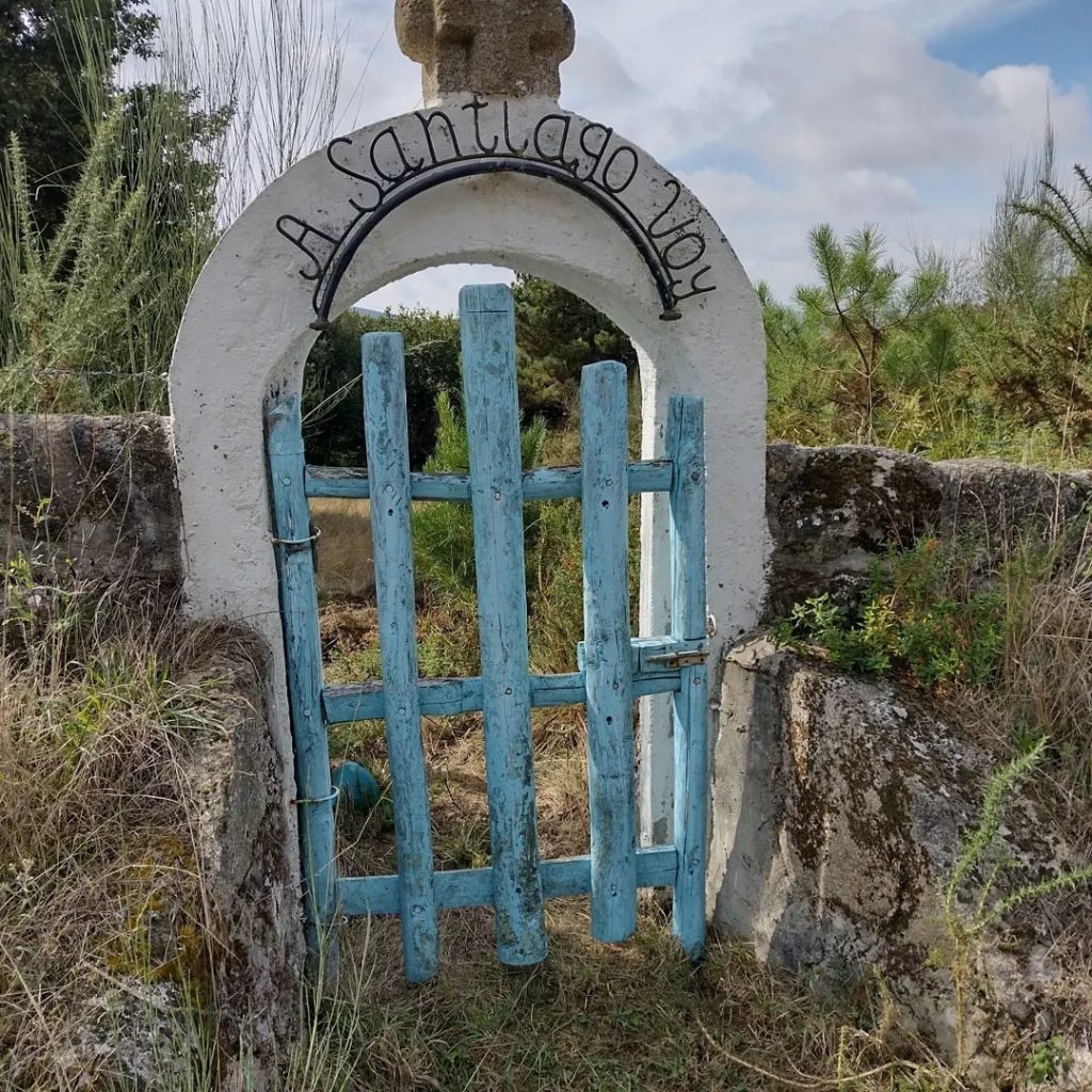 Puerta en un entorno rural con la leyenda "A Santiago voy" en el arco superior.
