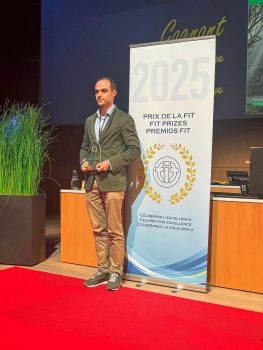 Miguel Pérez Bornstein posa con el premio FIT otorgado a La Linterna del Traductor junto a una banderola con el texto "Premios FIT 2025". 